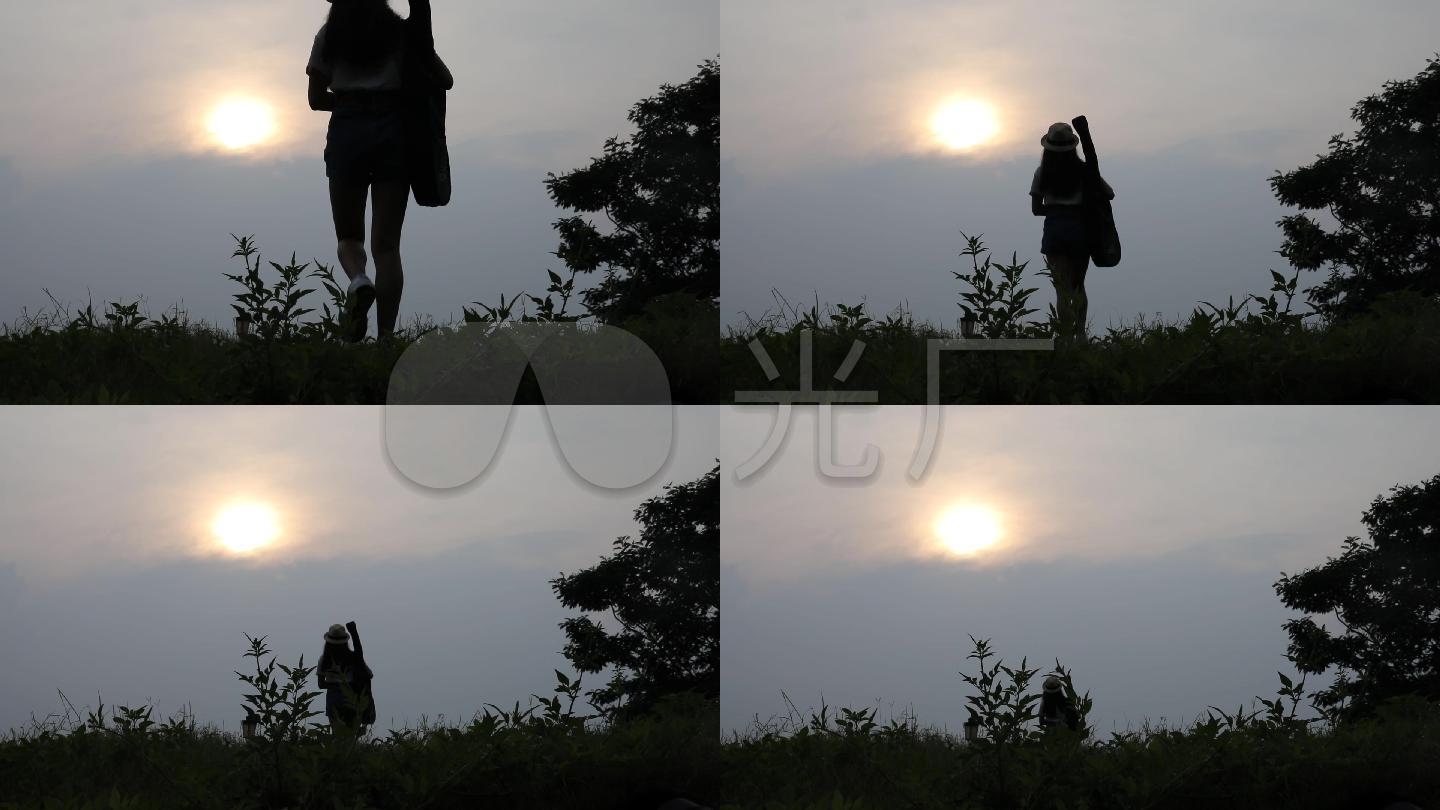 女孩背着吉他在夕阳下走下山