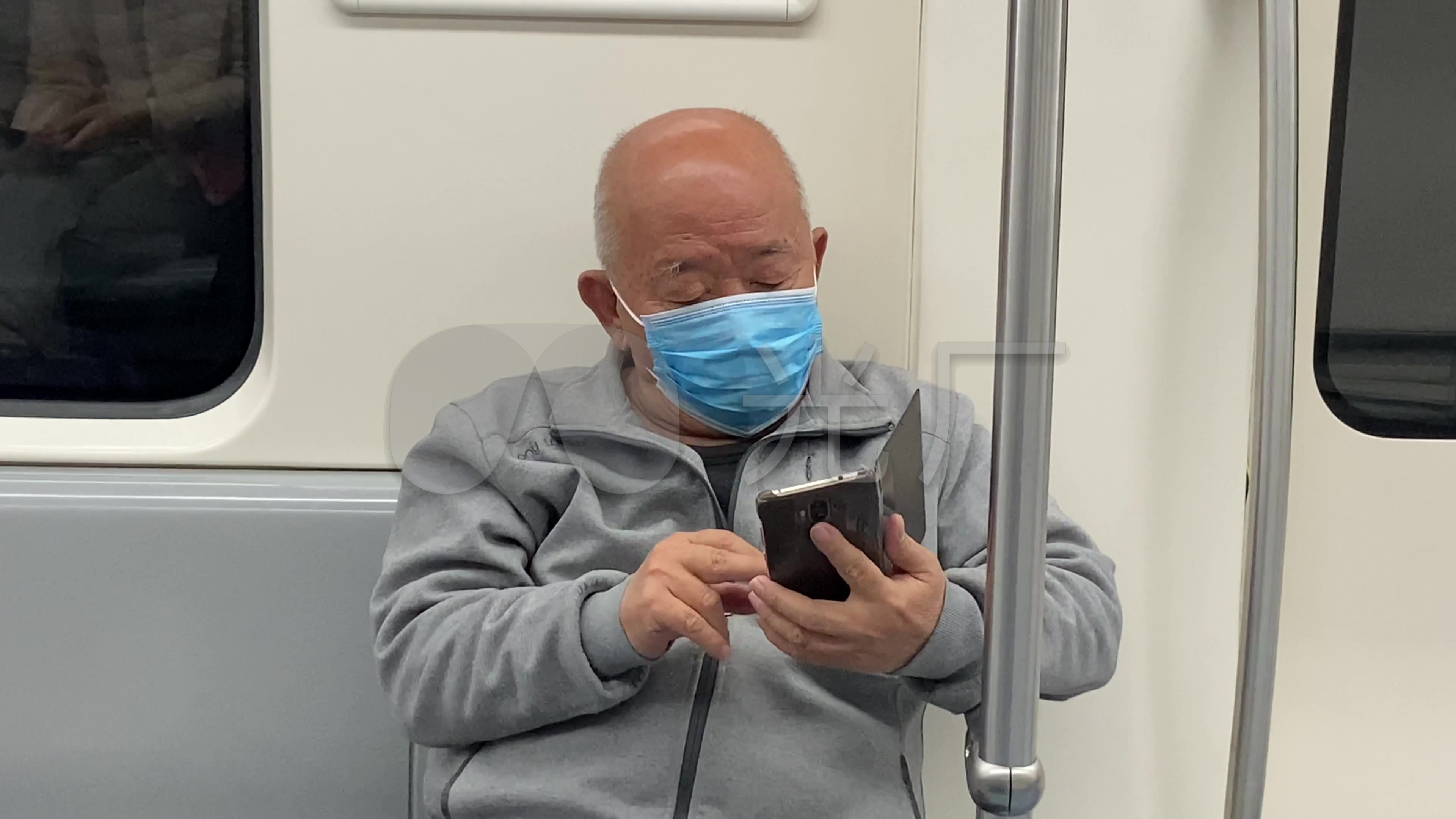 疫情期间一位老人在地铁上认真看手机