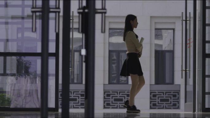 美女大学生怀抱书本走过走廊