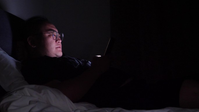 失眠晚上躺在床上玩手机的男人