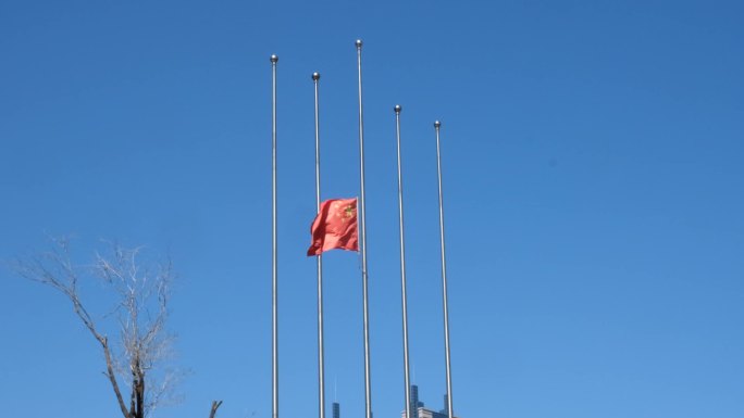 蓝天背景下降半旗的旗杆和飘扬的红旗