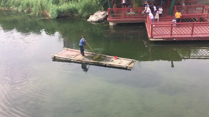 保洁工人站在竹筏在湖面上清理杂物垃圾