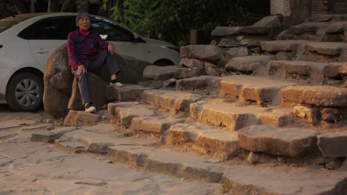 黄昏下石板台阶旁的老年妇女