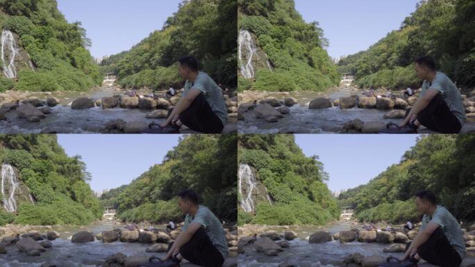 单身汉寂寞的坐在瀑布下的小溪边