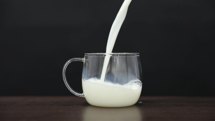 黑色背景下牛奶缓慢倒入玻璃杯升格素材