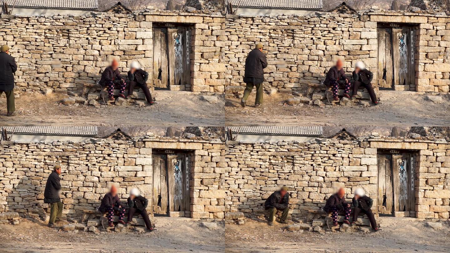 坐在石头房子前晒太阳聊天的农村老人