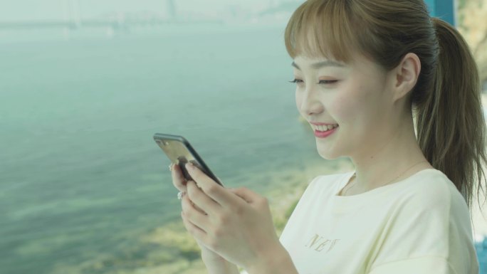 年轻的女士在海边用手机给朋友发消息