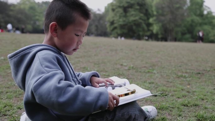 【原创实拍】坐在草坪看书的小男孩