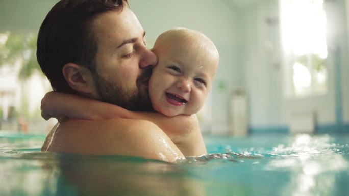 可爱的小宝宝和他的爸爸在游泳池里上游泳课