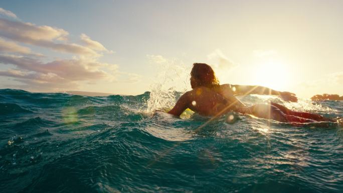 在日落时，冲浪者划过蓝色的海浪慢动作