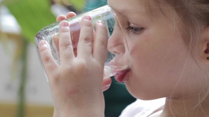 一个可爱的小女孩用玻璃杯喝纯净水