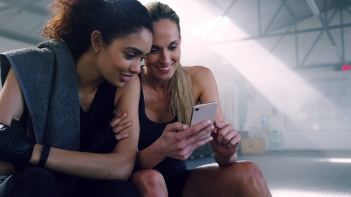 两个年轻女子在健身房一起看手机