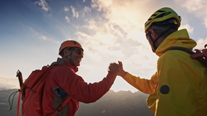 日落时分，两位登山者在山顶握手