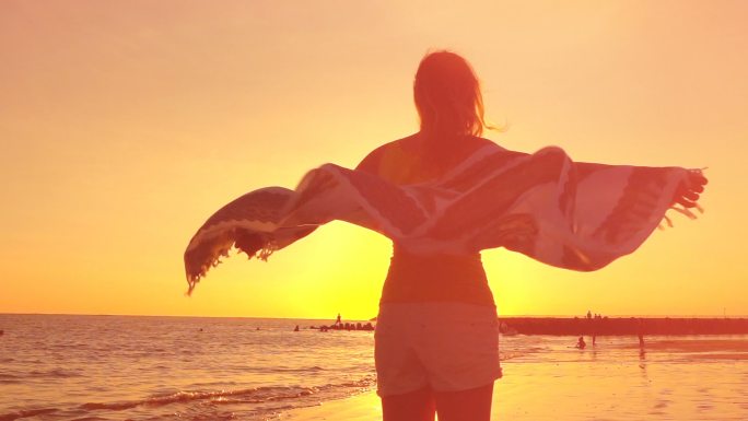 戴着太阳镜和飘动围巾的女孩在沙滩上旋转