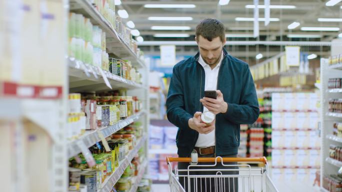 在超市里，帅哥用智能手机查看罐头标签