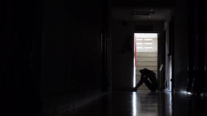 一个女孩黑暗中靠在老公寓的墙坐着