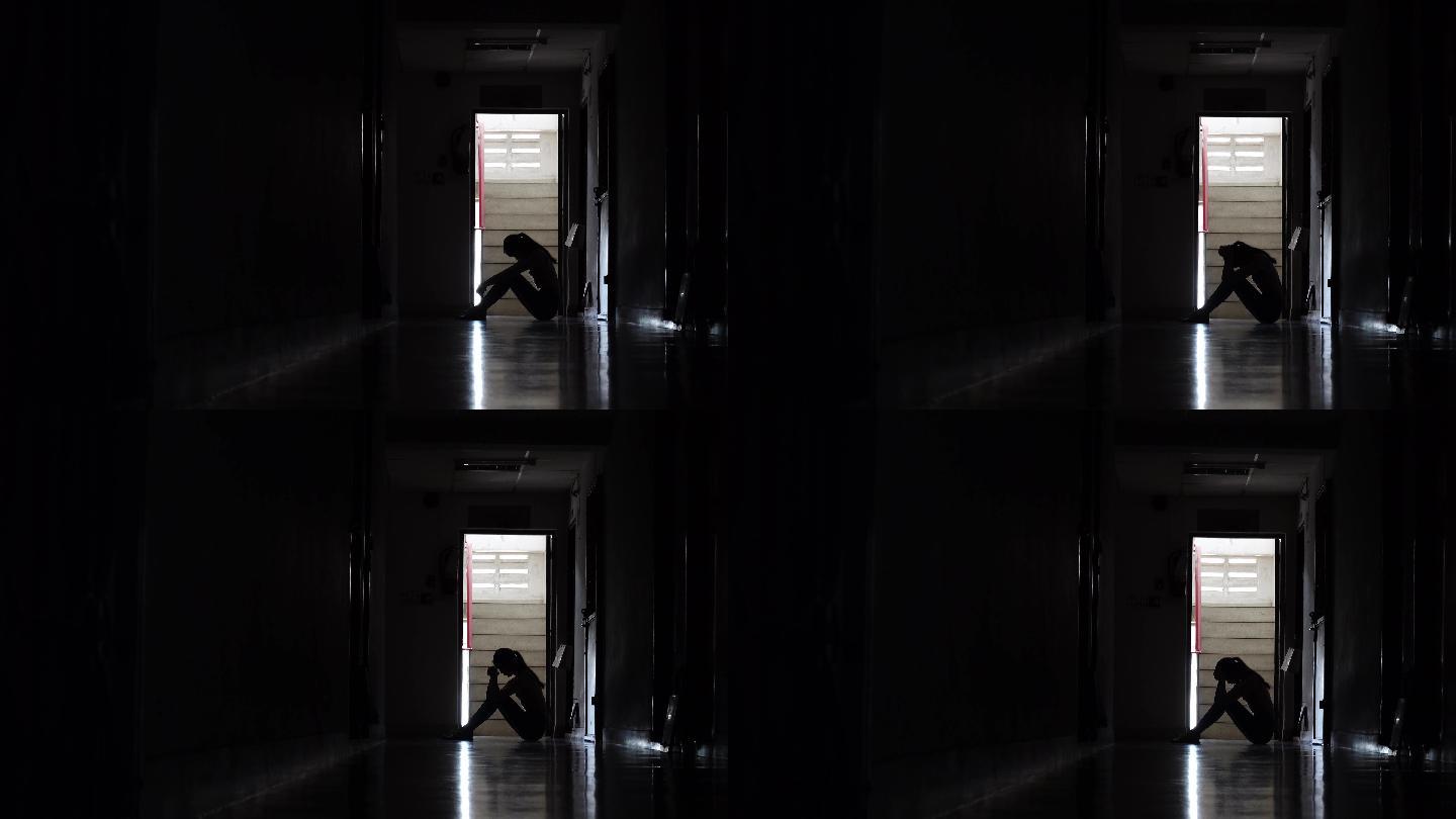 一个女孩黑暗中靠在老公寓的墙坐着