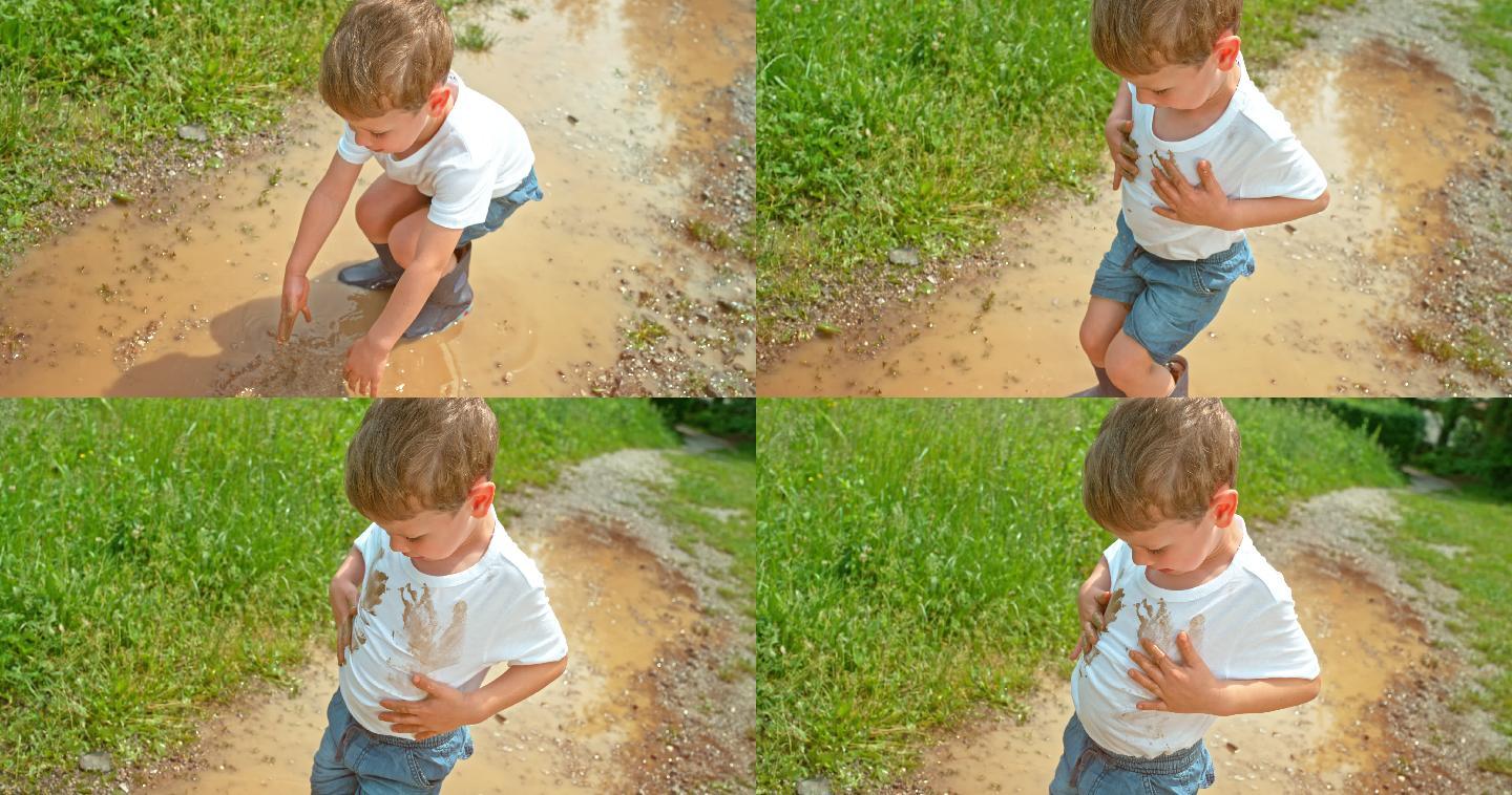 小男孩把手放在泥泞的水坑里