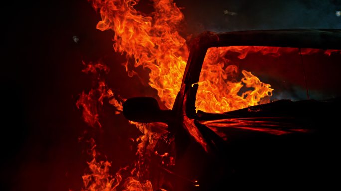 一辆破旧的汽车在夜间被滚滚的火焰吞没