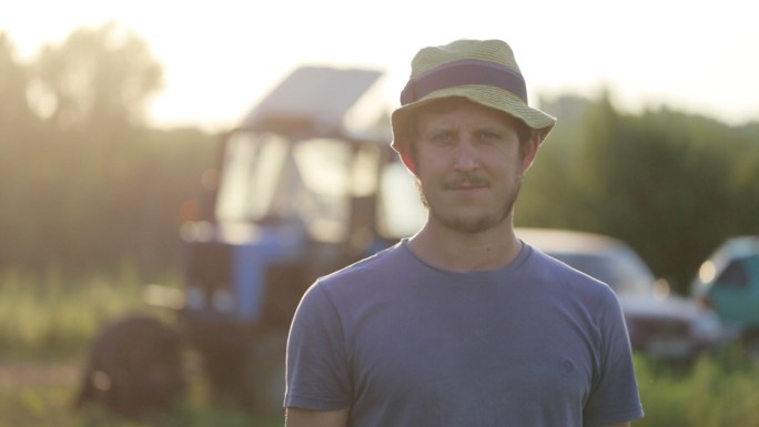 戴帽子的年轻农民站在有机农场的田地里微笑