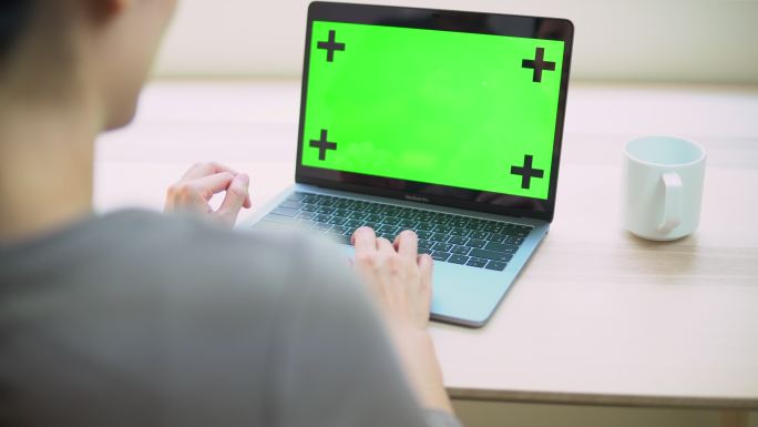 女人在家里用绿色屏幕的笔记本电脑打字