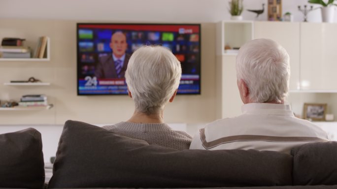 一对老年夫妇坐在沙发上看电视新闻