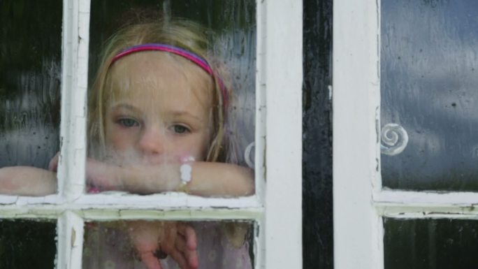 一个女孩透过小屋窗户看着外面的大雨