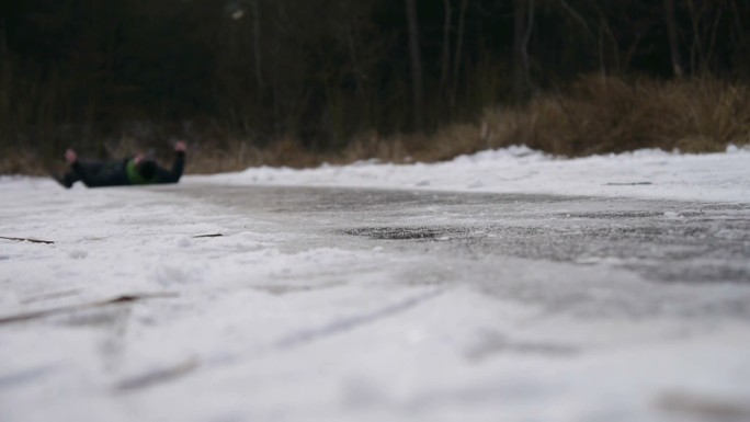 年轻人滑倒在结冰的湖面上