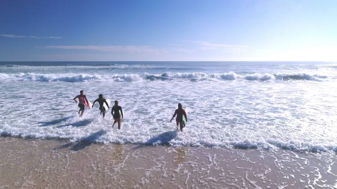 四个冲浪者拿着冲浪板跑进海里。