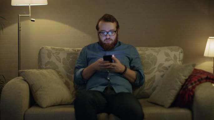 男人坐在客厅的沙发上玩手机