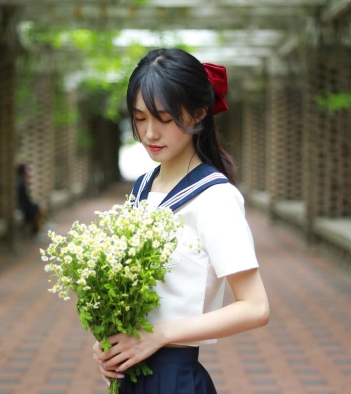 穿着JK服水手服的女孩拿着书本和花朵