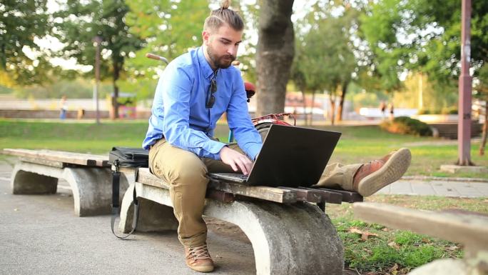 男子坐在公园长凳上用笔记本电脑工作