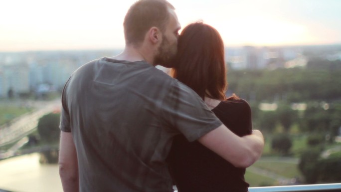 年轻夫妇拥抱在夕阳下的城市背景