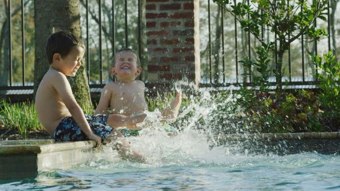 两个小男孩坐在游泳池边踢水
