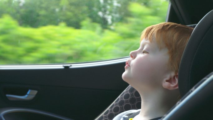 男孩在公路旅行中安全地坐在汽车座椅上