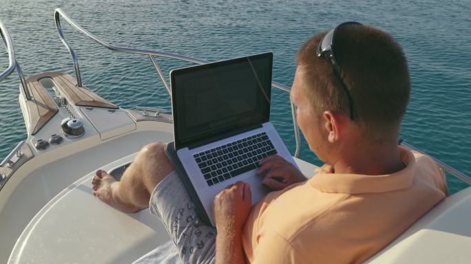 男人坐在船上操作笔记本电脑