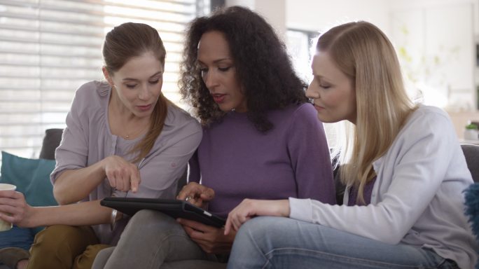 三位女性在使用数字平板电脑时交谈