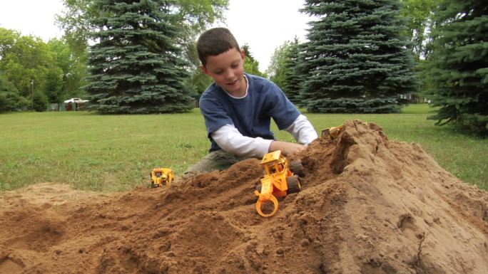 男孩在沙堆上玩卡车玩具