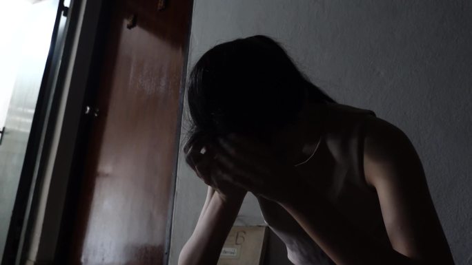 一个悲伤的年轻女孩靠在老公寓的墙上