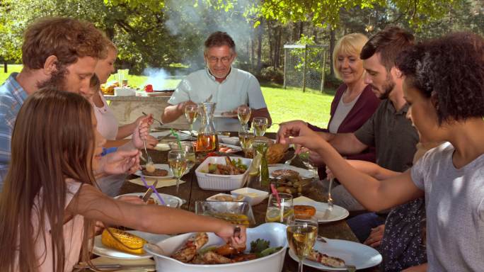 一个家庭坐在餐桌旁野餐，享受烤肉的食物。