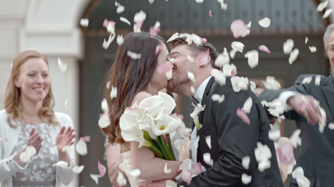 宾客向亲吻的新婚夫妇投掷花瓣