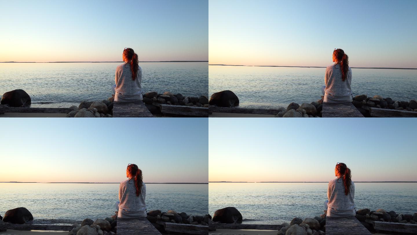 女人在岩石湖边的木码头上看日落