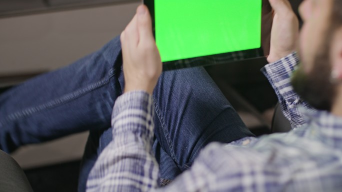 坐在沙发上玩绿屏平板电脑的男人
