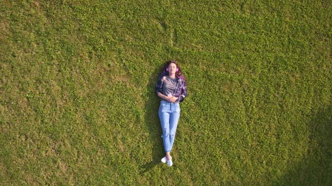 无人机拍摄的女子在草地上听音乐的画面