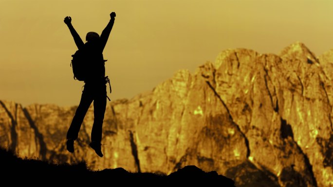 男性攀岩运动员在山顶上胜利跳跃