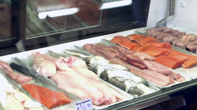 一名女工把手伸进海鲜市场展示柜取出鱼片