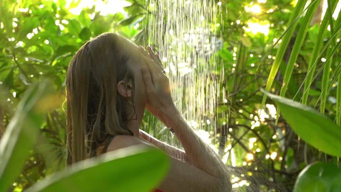 年轻苗条的女人在热带花园里享受清爽的淋浴
