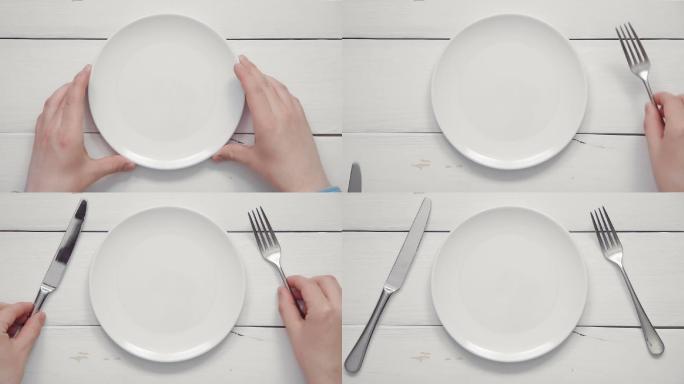 男性双手将白色盘子和餐具放在白色餐桌上