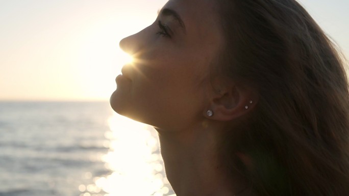 一个年轻的女子面对阳光站在海边