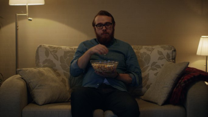 一个男人坐在客厅的沙发上吃爆米花